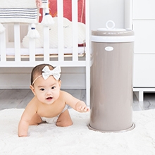 Baby next to diaper disposal bin and baby changing station in nursery
