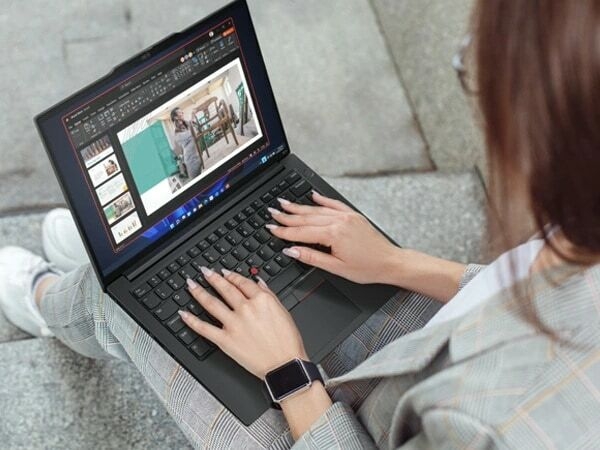 Over-the-shoulder, close-up view of person sitting on concrete stairs, holding ThinkPad E14 Gen 5 (14″ Intel) laptop in their lap, with both hands on keyboard, looking at slideshow on the display