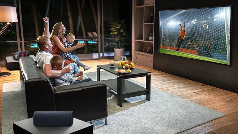 A family are sitting on a couch while watching a soccer game.