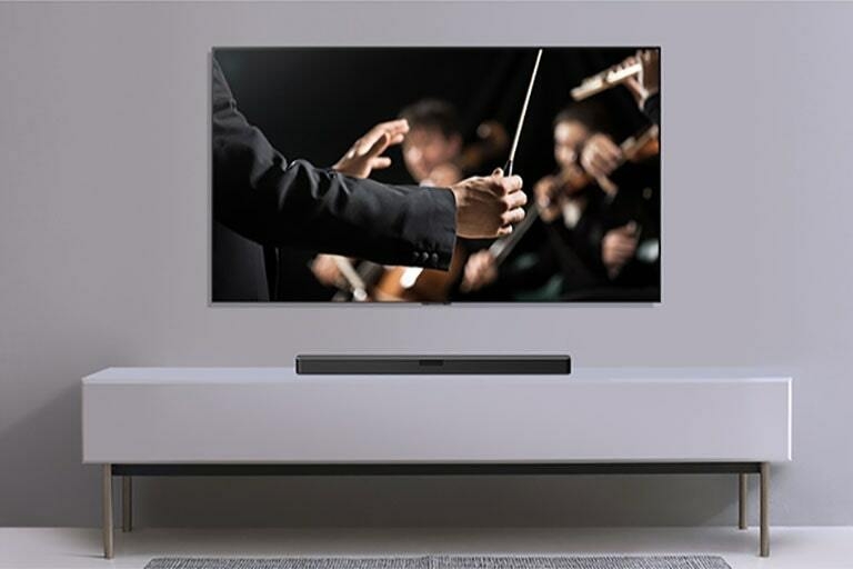 A TV is shown on a gray wall and LG Soundbar below it on a gray shelf. TV shows a conductor conducting an orchestra.
