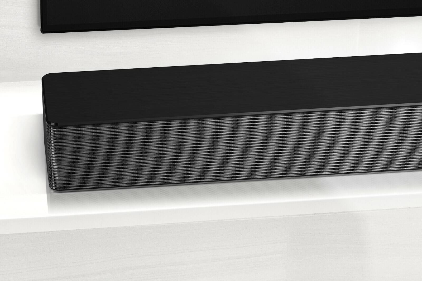 Close-up of LG Soundbar left corner. Bottom left side of TV is also visible. 